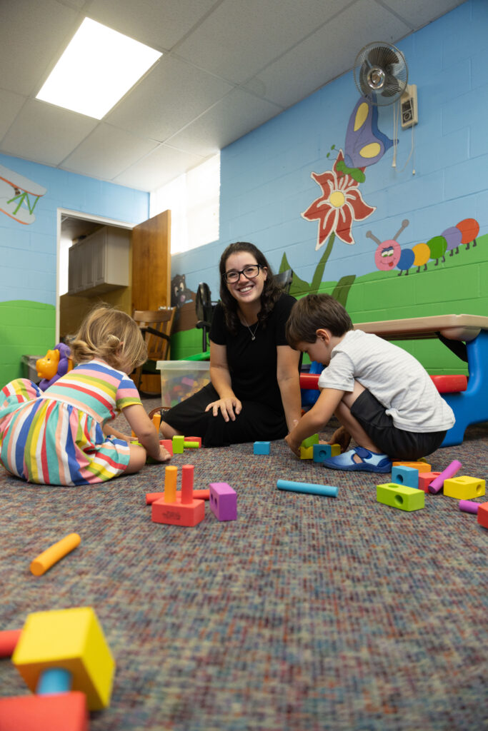Katy Duckstein sits smiling as two children play with blocks in her Pennsylvania hybrid homeschool classroom