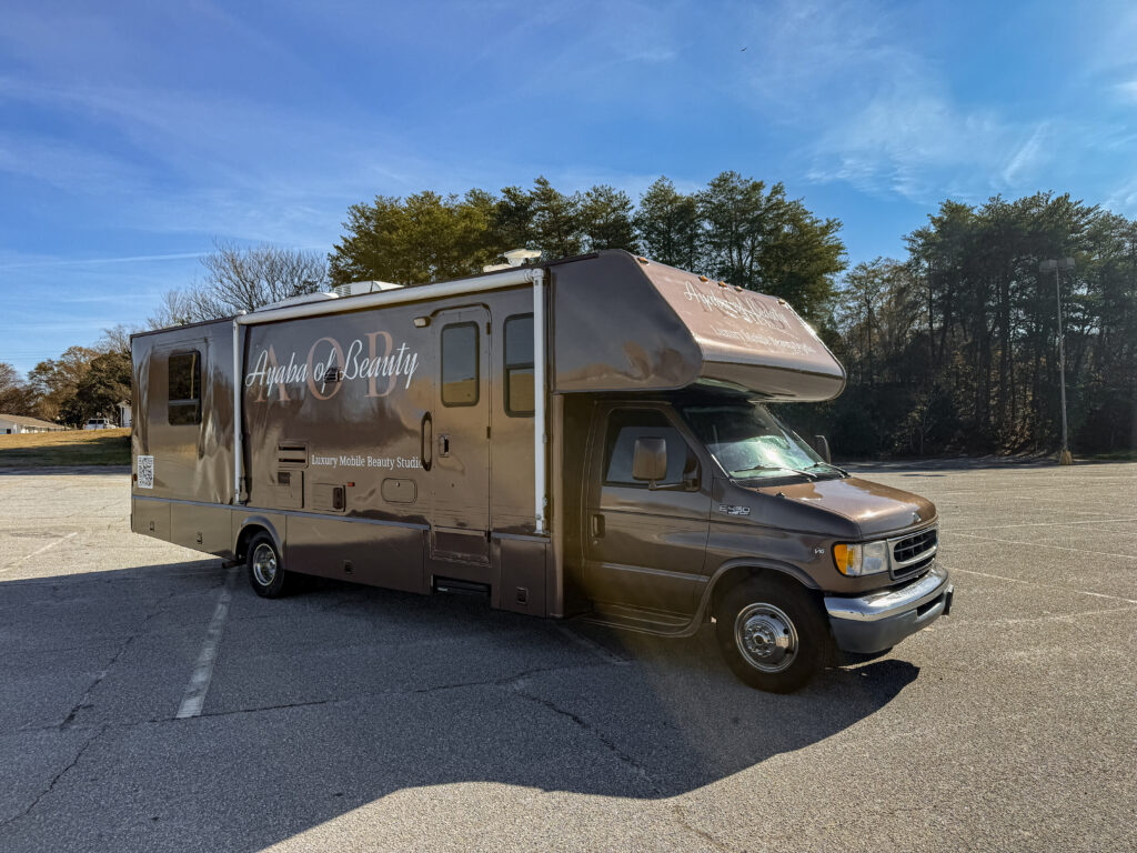 Brown RV branded Ayaba of Beauty, Brandi's luxury mobile beauty salon, parked in a lot