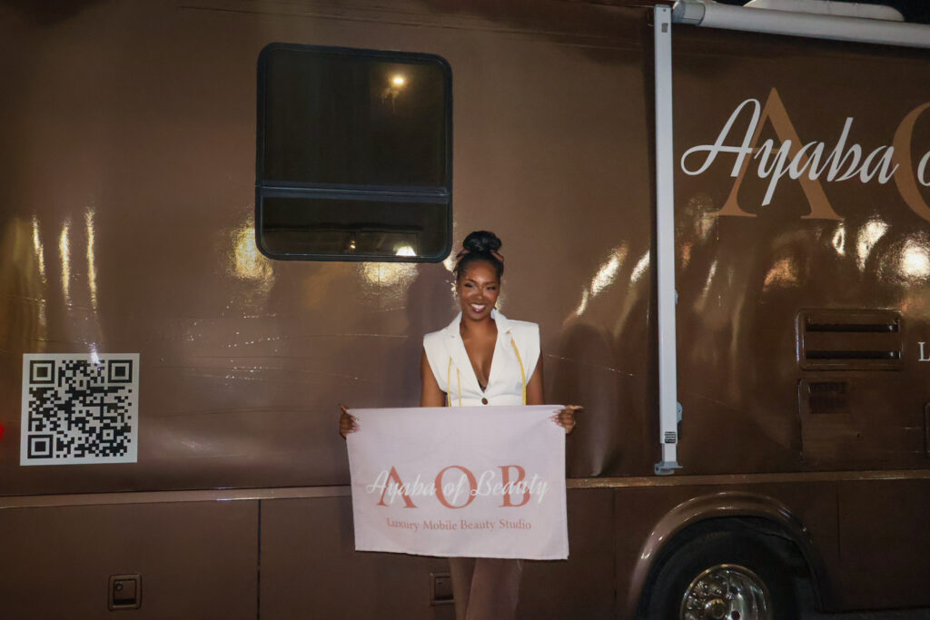 Brandi smiling, holding an Ayaba of Beauty sign in front of her mobile beauty salon