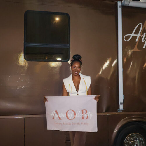 Brandi smiling, holding an Ayaba of Beauty sign in front of her mobile beauty salon