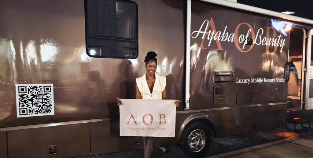 Brandi holding an Ayaba of Beauty banner beside her mobile beauty studio vehicle at night