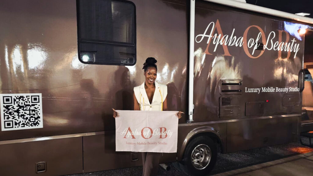 Brandi holding an Ayaba of Beauty banner beside her mobile beauty studio vehicle at night