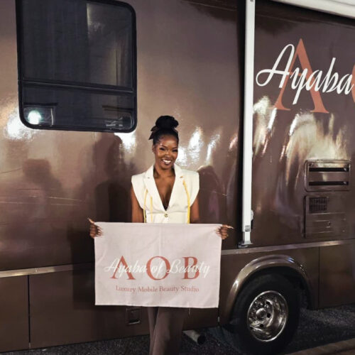 Brandi holding an Ayaba of Beauty banner beside her mobile beauty studio vehicle at night