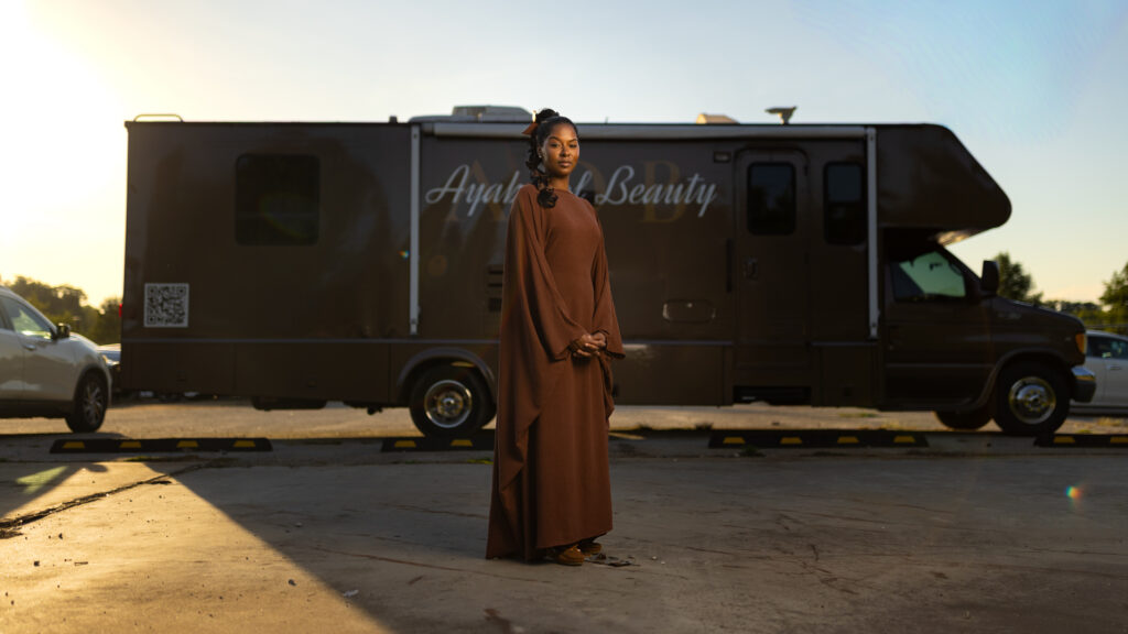 Woman stands in a flowing dress in front of an Ayah Beauty mobile salon vehicle