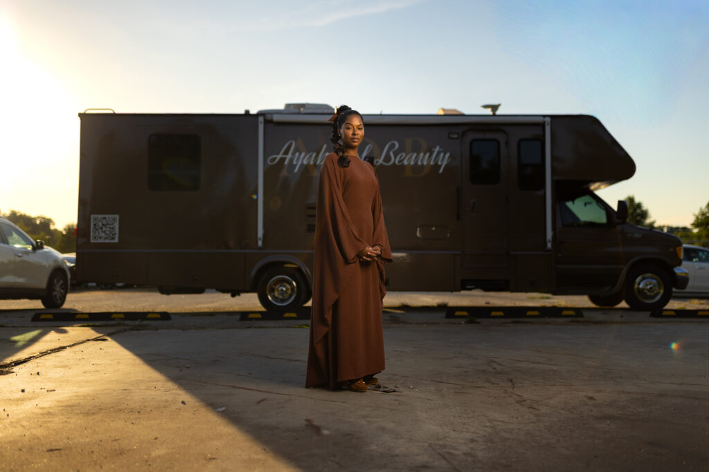Woman stands in a flowing dress in front of an Ayah Beauty mobile salon vehicle