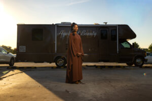 Woman stands in a flowing dress in front of an Ayah Beauty mobile salon vehicle