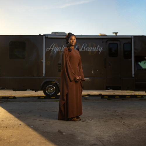Woman stands in a flowing dress in front of an Ayah Beauty mobile salon vehicle