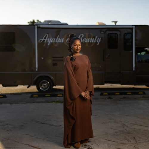Woman stands in front of Ayaba Beauty mobile salon RV parked in a lot