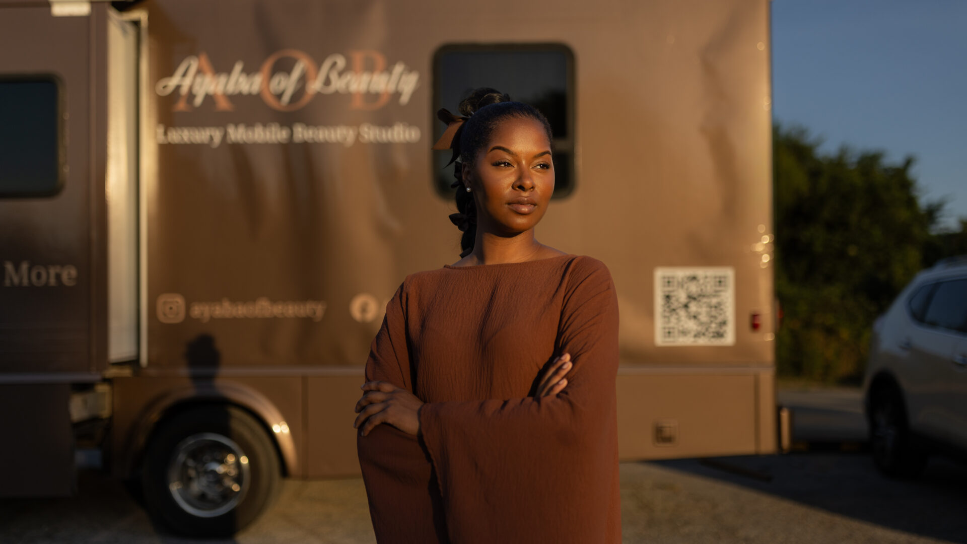Woman with arms crossed stands before the Ayaba of Beauty mobile beauty studio truck