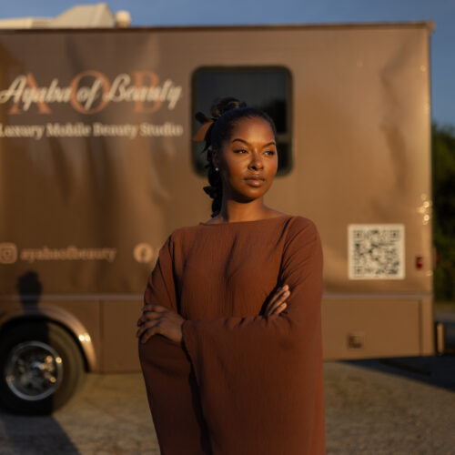 Woman with arms crossed stands before the Ayaba of Beauty mobile beauty studio truck