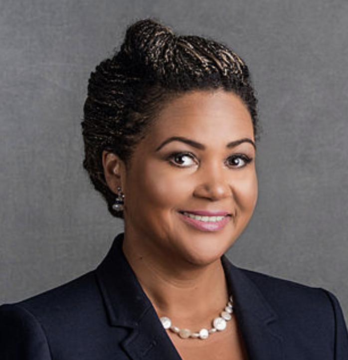 Woman in dark blazer and pearl necklace smiles in professional headshot portrait
