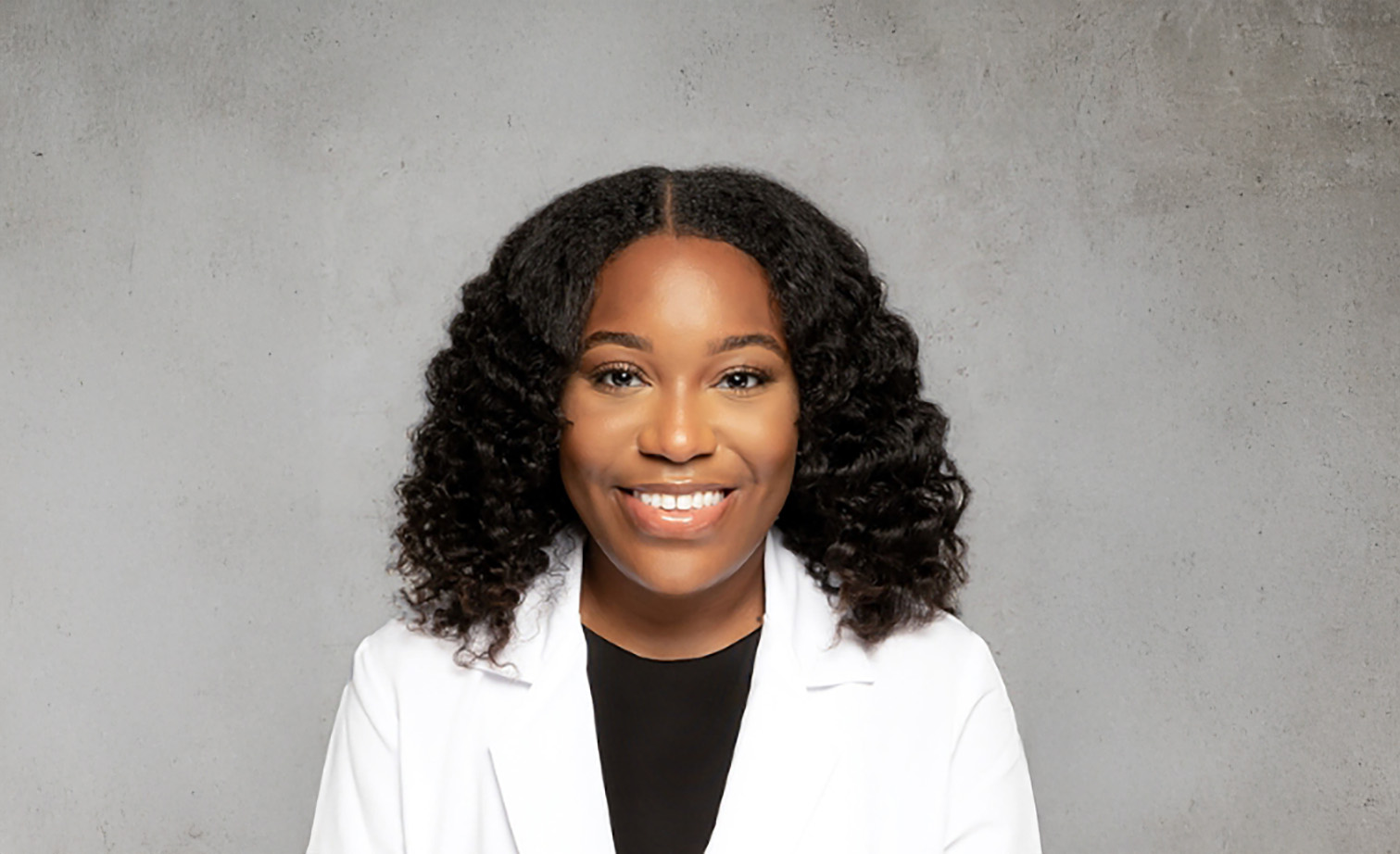 Woman with curly hair smiling in white blazer, professional headshot for Vash Beauty Labs
