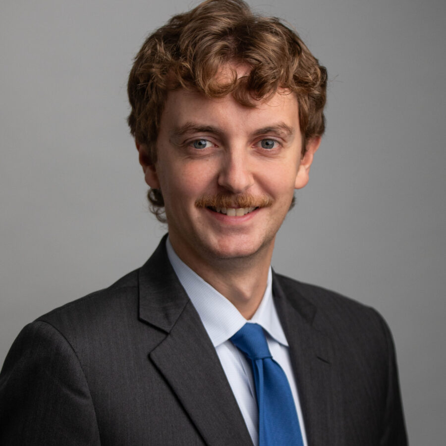 Headshot of a man with a mustache in a dark suit and blue tie