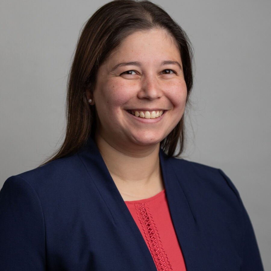 Woman with long brown hair smiling in navy blazer and red top, professional headshot