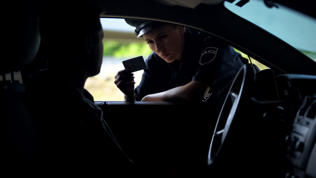 Police officer examines a driver's license through a car window during traffic stop