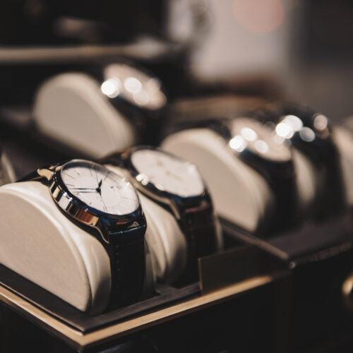 Rows of wristwatches with round faces displayed on cushions in a store case