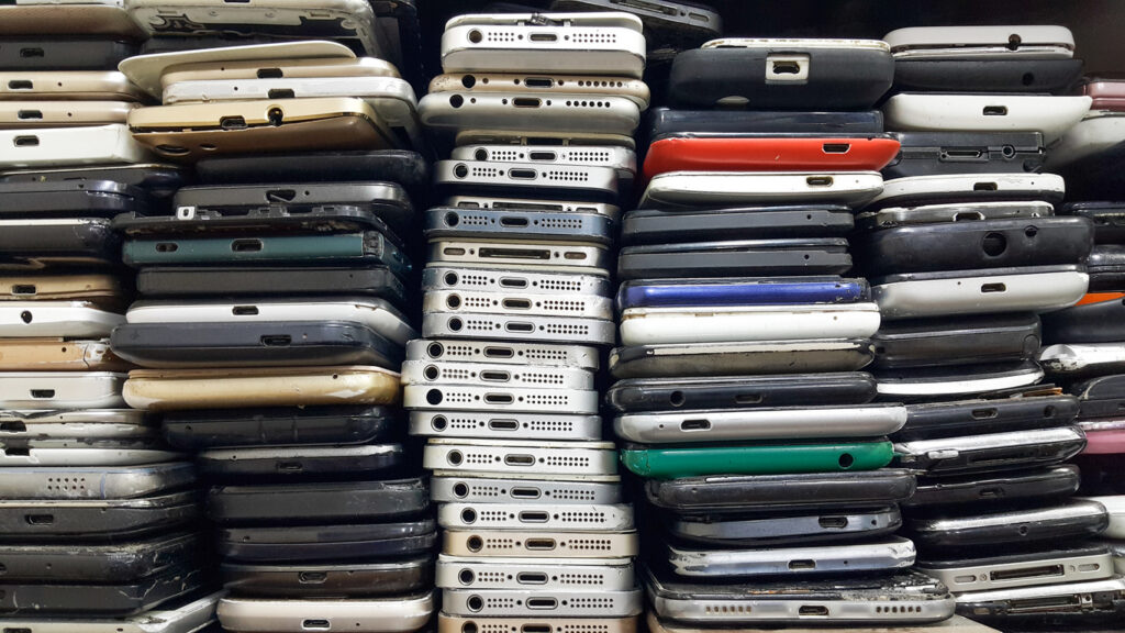 Stacks of used smartphones piled together, showing worn cases and charging ports