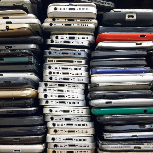 Stacks of used smartphones piled together, showing worn cases and charging ports