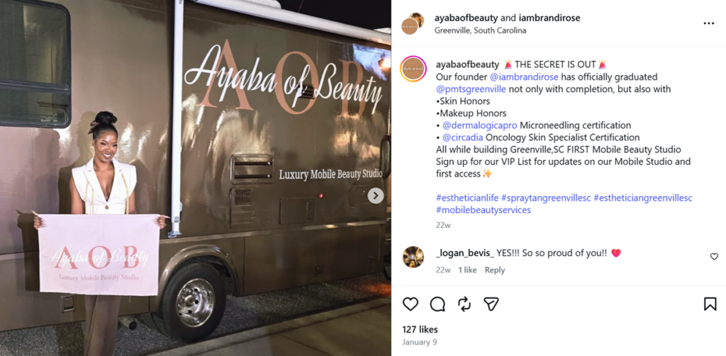 Woman holds Ayaba of Beauty sign beside branded mobile beauty studio vehicle at night