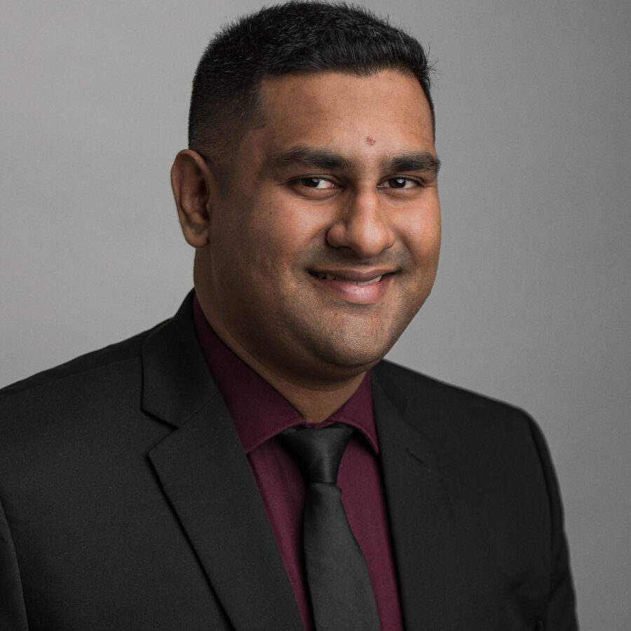 Man in dark suit and maroon shirt smiling in a professional headshot portrait