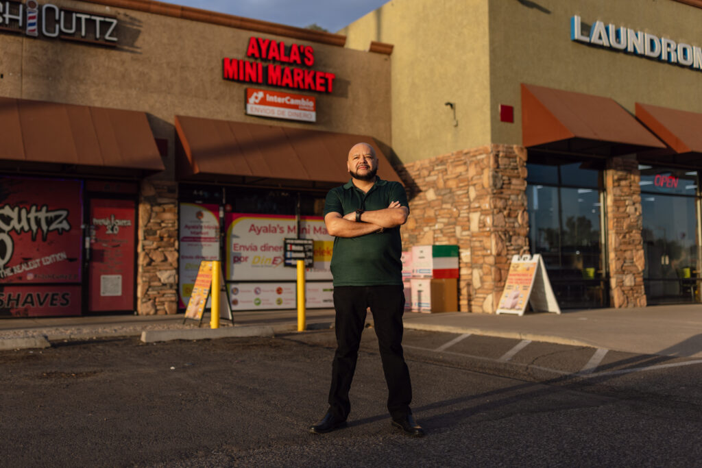 Mario Ayala stands arms crossed outside Ayala's Mini Market storefront in Glendale, Arizona.
