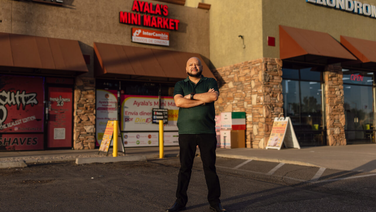 Mario Ayala stands arms crossed outside Ayala's Mini Market storefront in Glendale, Arizona.