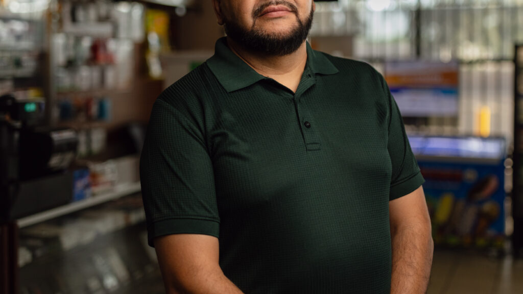 Mario Ayala, torso view in green polo, standing inside Ayala's Mini Market in Glendale, Arizona