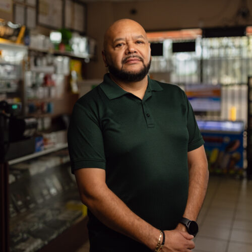 Mario Ayala, torso view in green polo, standing inside Ayala's Mini Market in Glendale, Arizona