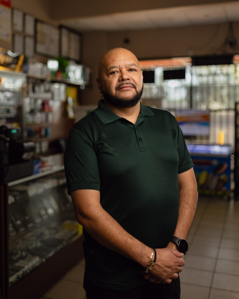 Mario Ayala, torso view in green polo, standing inside Ayala's Mini Market in Glendale, Arizona