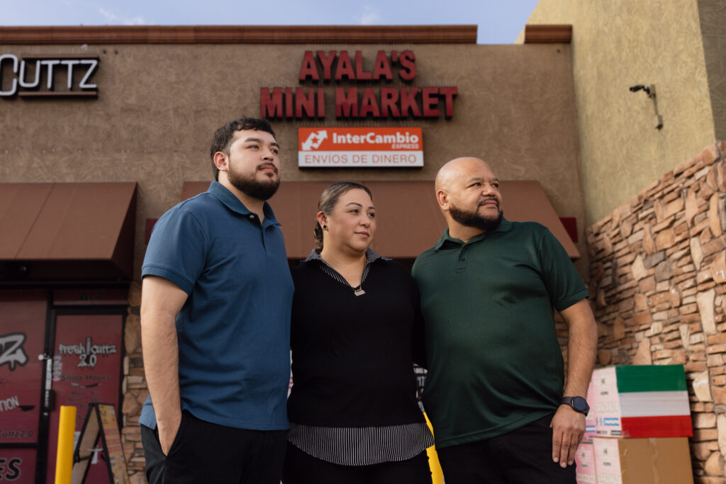 Three people stand outside Ayala's Mini Market beneath an InterCambio Express money transfer sign
