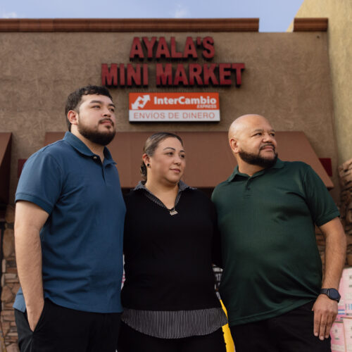 Three people stand outside Ayala's Mini Market beneath an InterCambio Express money transfer sign
