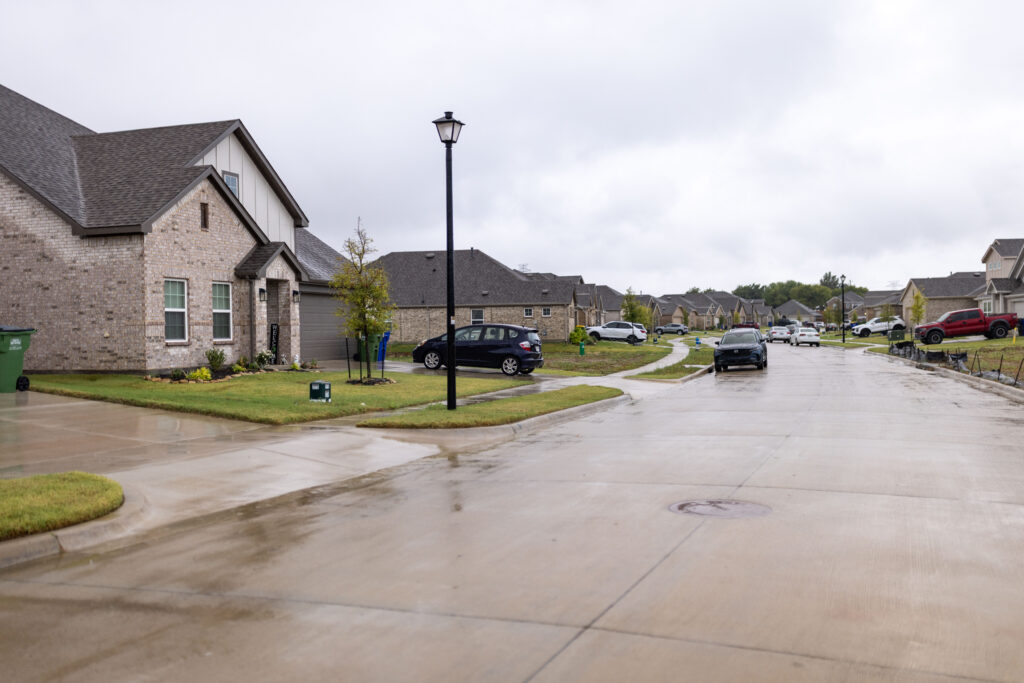 Rainy suburban street in Venus, Texas, with brick homes, driveways, and parked cars