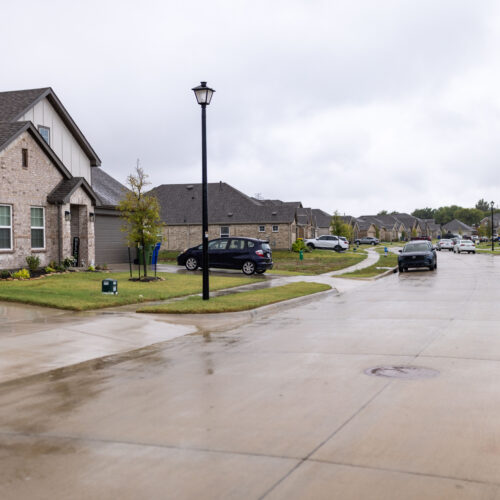Rainy suburban street in Venus, Texas, with brick homes, driveways, and parked cars