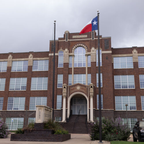Brick former high school building, now Johnson County Courthouse, with American and Texas flags