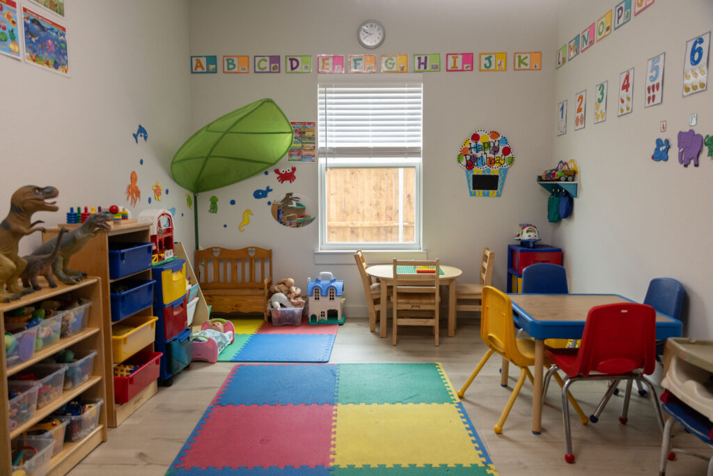 Colorful daycare classroom with alphabet decor, foam mats, toy shelves, and kid-sized tables and chairs