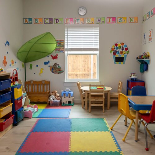Colorful daycare classroom with alphabet decor, foam mats, toy shelves, and kid-sized tables and chairs