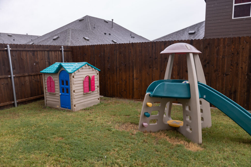 Toy playhouse and slide in fenced backyard of Rosi Paredes' home daycare in Venus, Texas
