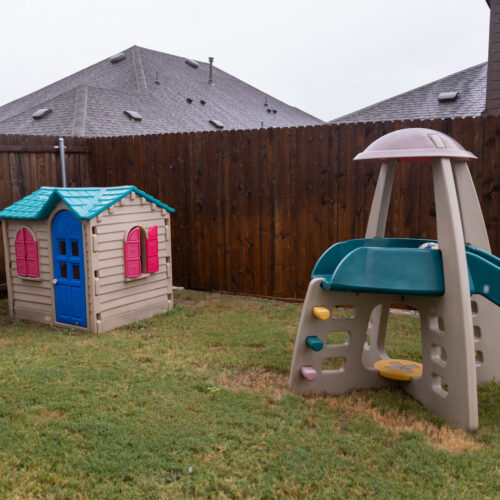 Toy playhouse and slide in fenced backyard of Rosi Paredes' home daycare in Venus, Texas