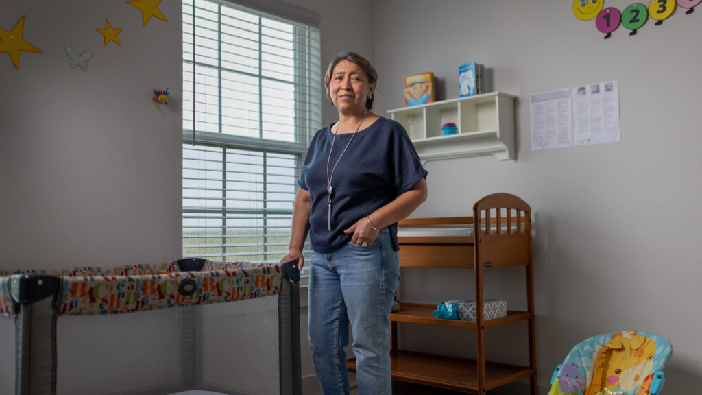 Rosi Paredes stands in her home daycare nursery with a crib, changing table, and playful wall decor