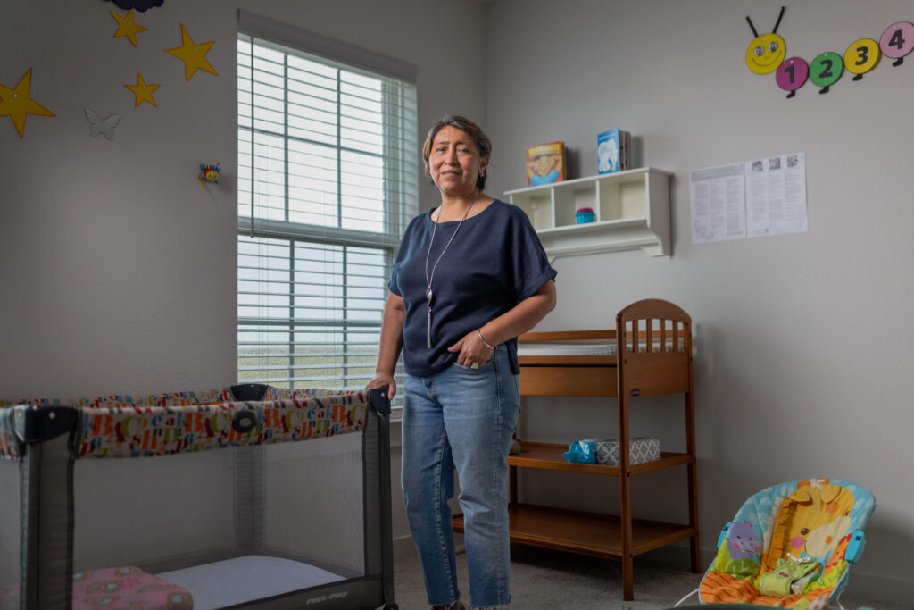 Rosi Paredes stands in her home daycare nursery with a crib, changing table, and playful wall decor