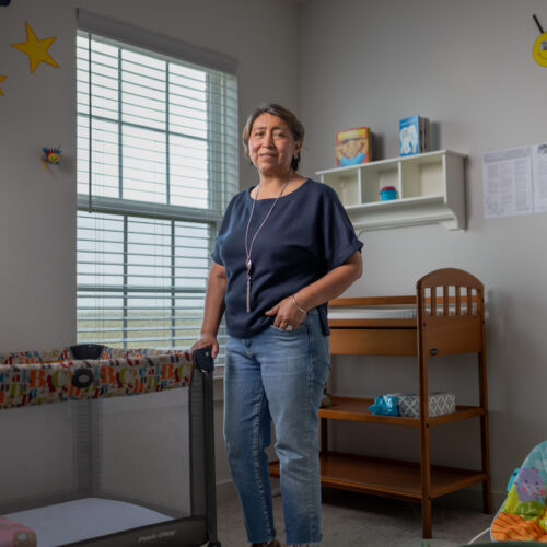 Rosi Paredes stands in her home daycare nursery with a crib, changing table, and playful wall decor