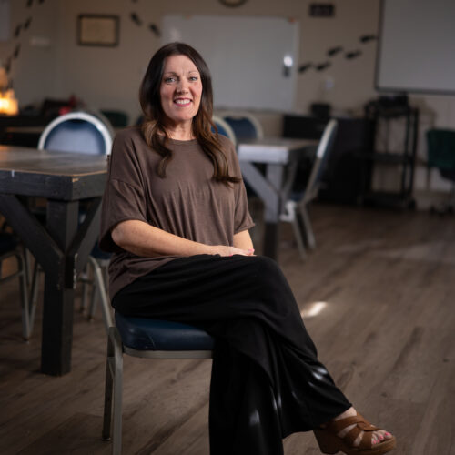 Woman with brown hair smiling, seated at a table in a casual indoor setting