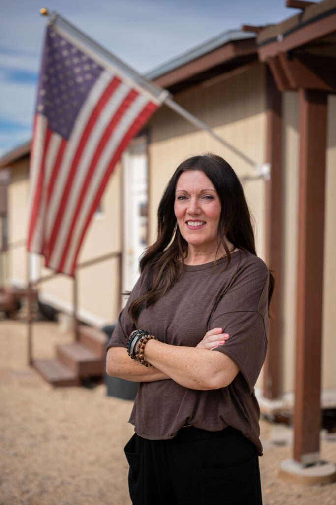Woman with arms crossed smiling outdoors near an American flag in Pinal, Arizona