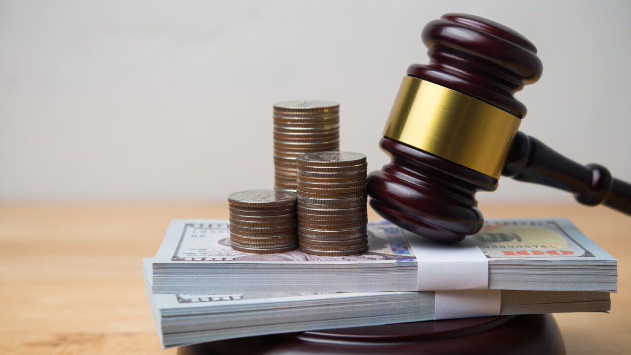 Gavel resting on stacked hundred-dollar bills and coin stacks, symbolizing fines and financial penalties