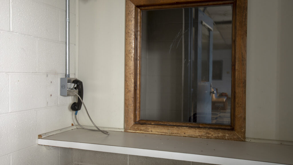 Wall-mounted phone beside glass window used by visitors to communicate with inmates in prison