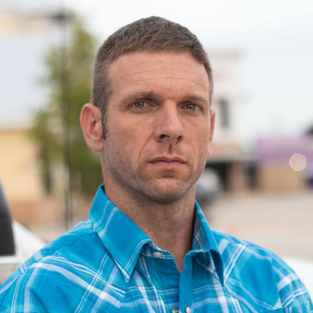 Man in blue plaid shirt stands outdoors, looking off to the side